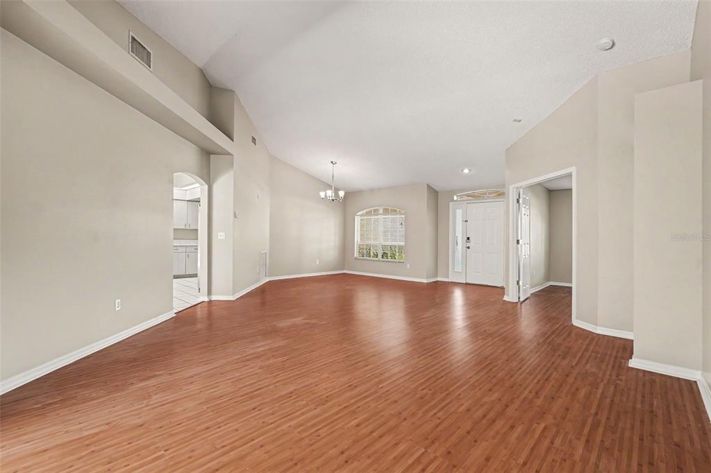 An empty living room features high vaulted ceilings, light-colored walls, and wood-look laminate flooring — 2909 STARMOUNT DRIVE, VALRICO, FL