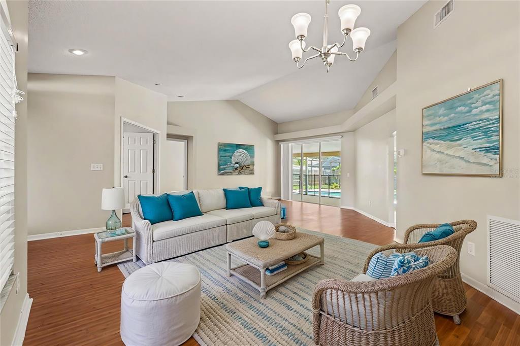 A living room features a vaulted ceiling, wicker furniture, blue accents, and sliding glass doors — 2909 STARMOUNT DRIVE, VALRICO, FL