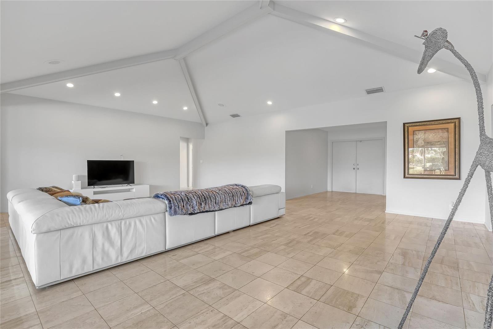 A spacious living room features white walls, vaulted ceilings, tile flooring, and a large sectional — 4989 Pineview Circle, Delray Beach FL 33445, DELRAY BEACH, FL