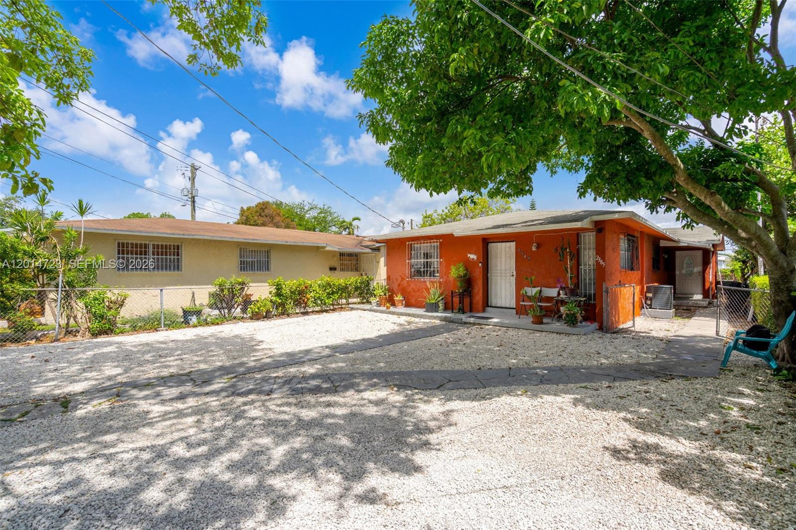 An orange house with a gravel driveway and a neighboring building under a blue sky — 2385 NW 32nd St, Miami FL 33142, MIAMI, FL