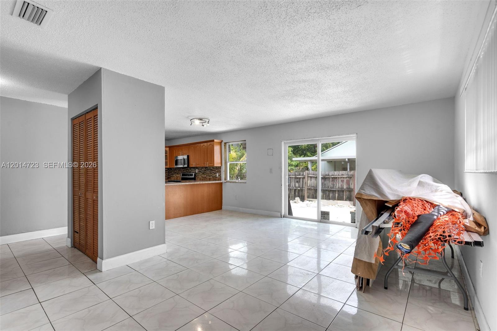 An open-concept living area features light tile flooring, gray walls, and an adjacent wooden kitchen — 2385 NW 32nd St, Miami FL 33142, MIAMI, FL