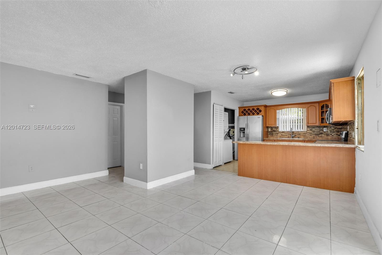 This open-concept kitchen and living area features light gray walls, tile flooring, and wood cabinetry — 2385 NW 32nd St, Miami FL 33142, MIAMI, FL