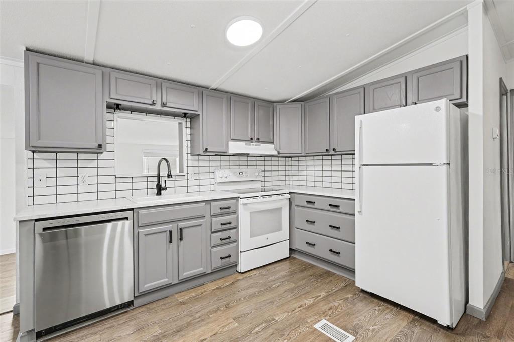 A kitchen features gray cabinets, white subway tile backsplash, stainless steel dishwasher, and white appliances — 9213 SALISBURY DRIVE, BROOKSVILLE, FL