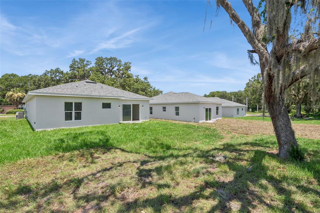 The exterior rear view of two newly constructed single-story houses with grassy yards and trees — 1328 MARSHALL DRIVE, LEESBURG, FL