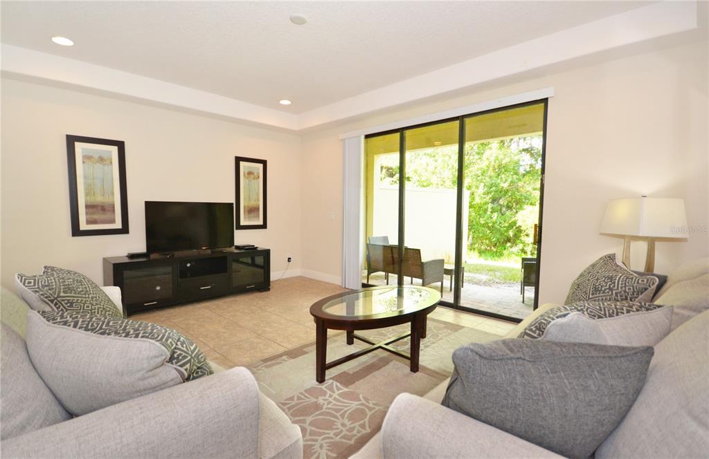 A living room features tile flooring, a television console, and sliding glass doors to a patio — 8211 ROSEVILLE ROAD, DAVENPORT, FL