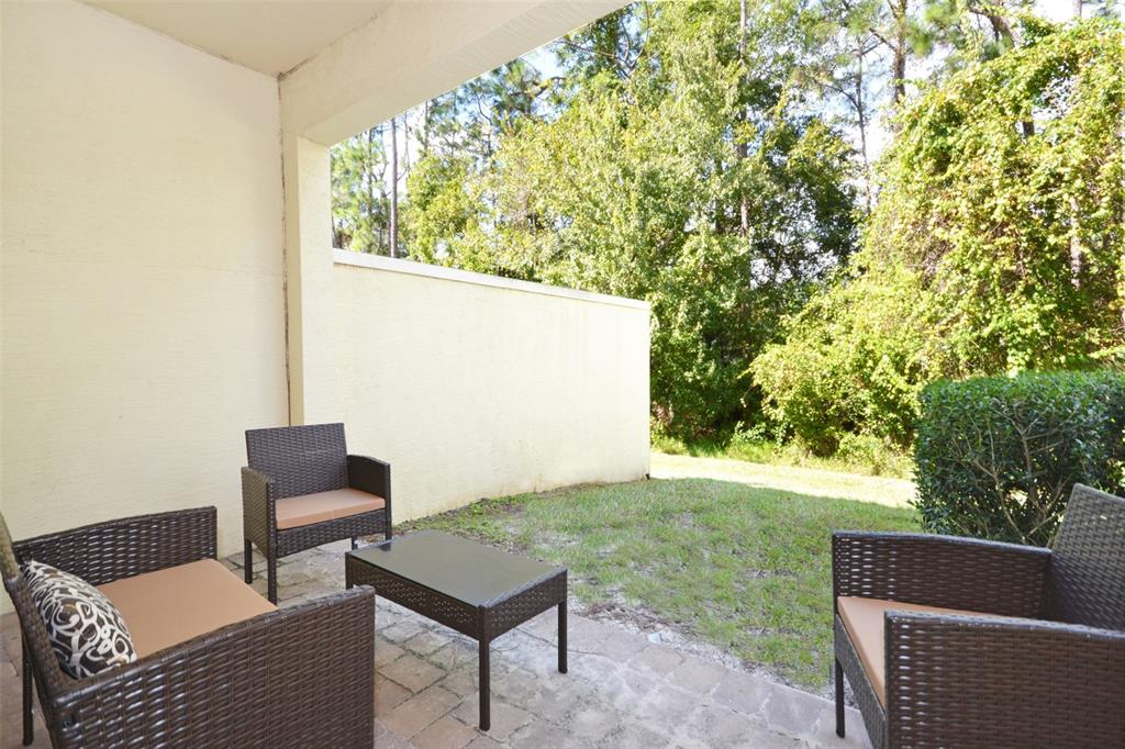 A patio with wicker furniture overlooks a grassy area and trees — 8211 ROSEVILLE ROAD, DAVENPORT, FL