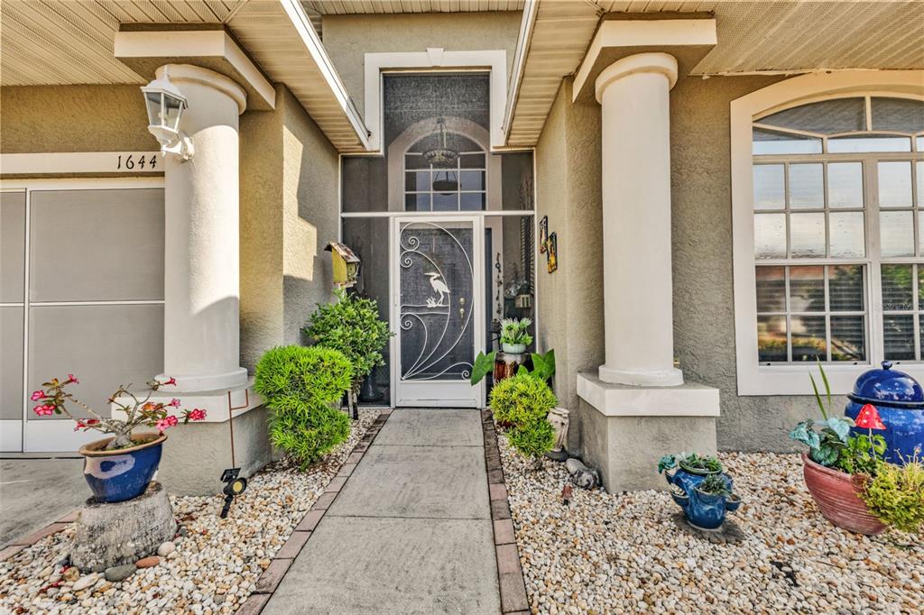 The exterior entrance features a concrete walkway, two white columns, and a decorative screen door — 1644 PALACE COURT, PUNTA GORDA, FL