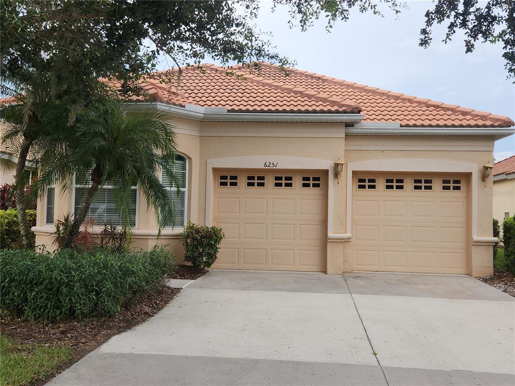 A single-story house with a beige stucco exterior, a tiled roof, and a two-car garage — 6251 WINGSPAN WAY, BRADENTON, FL