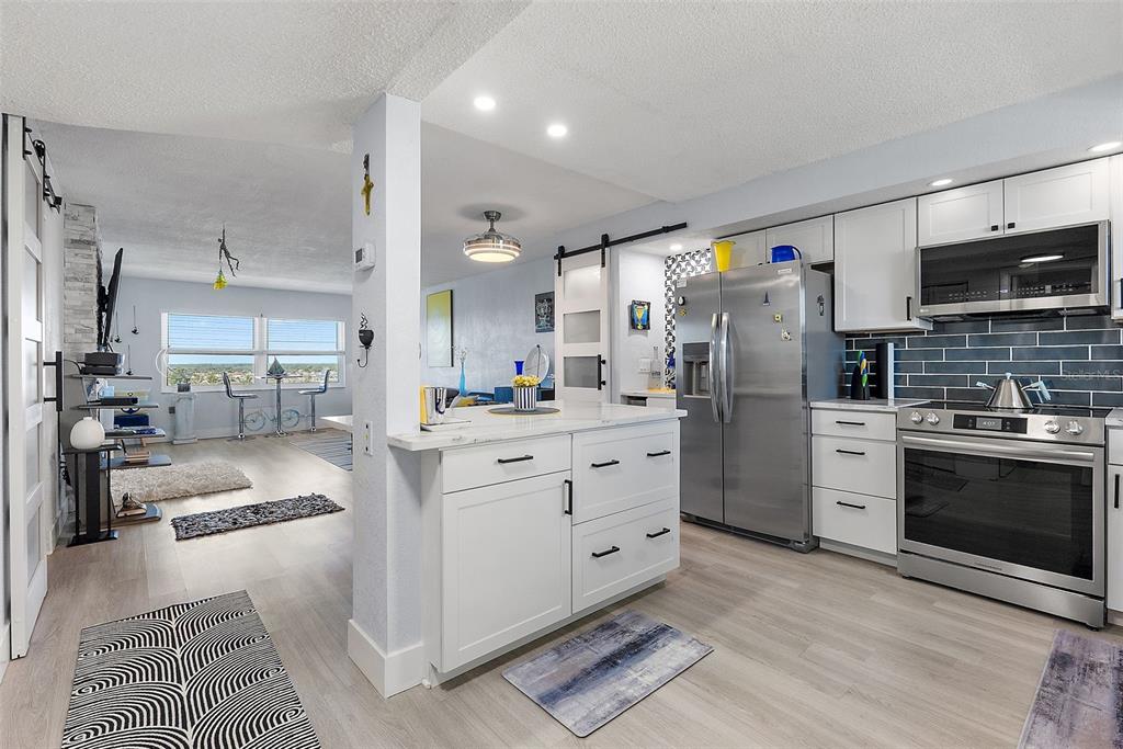 A kitchen with white cabinets and stainless steel appliances opens into a living area — 4725 COVE CIRCLE UNIT 704, ST PETERSBURG, FL