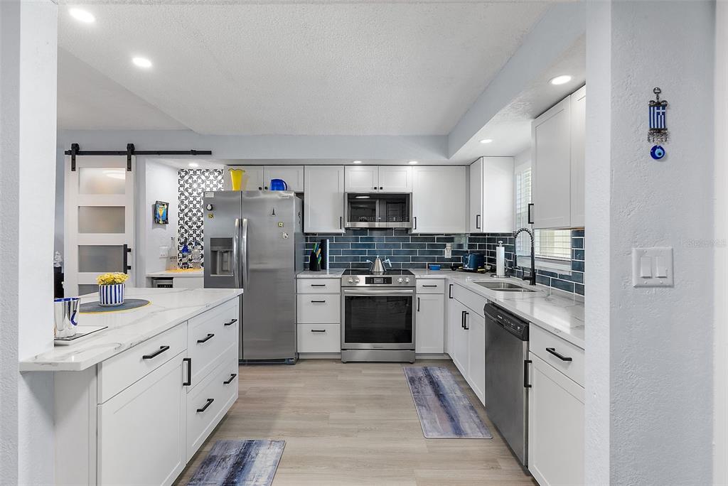 A modern kitchen features white cabinets, stainless steel appliances, a marble-topped island, and blue backsplash — 4725 COVE CIRCLE UNIT 704, ST PETERSBURG, FL