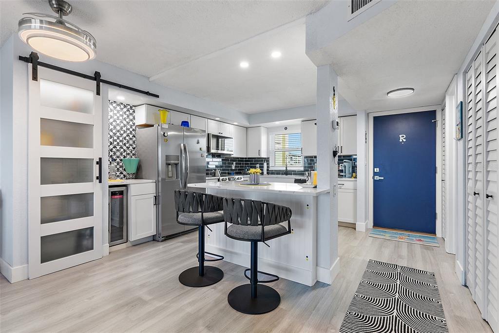 A kitchen features white cabinetry, a stainless steel refrigerator, a breakfast bar, and blue door — 4725 COVE CIRCLE UNIT 704, ST PETERSBURG, FL