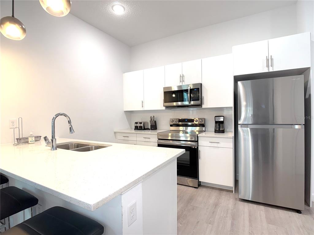 A modern kitchen features white cabinetry, stainless steel appliances, and a quartz-topped island — 332 FAMAGUSTA DRIVE, DAVENPORT, FL