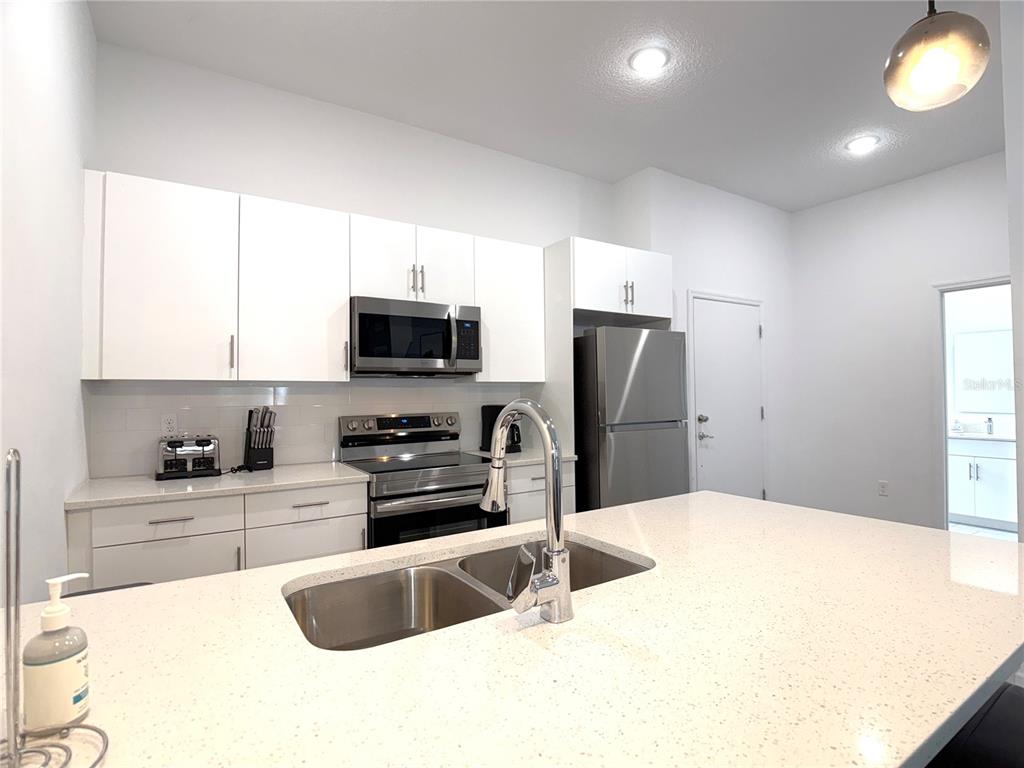 A modern kitchen features white cabinets, stainless steel appliances, and a quartz-topped island — 332 FAMAGUSTA DRIVE, DAVENPORT, FL