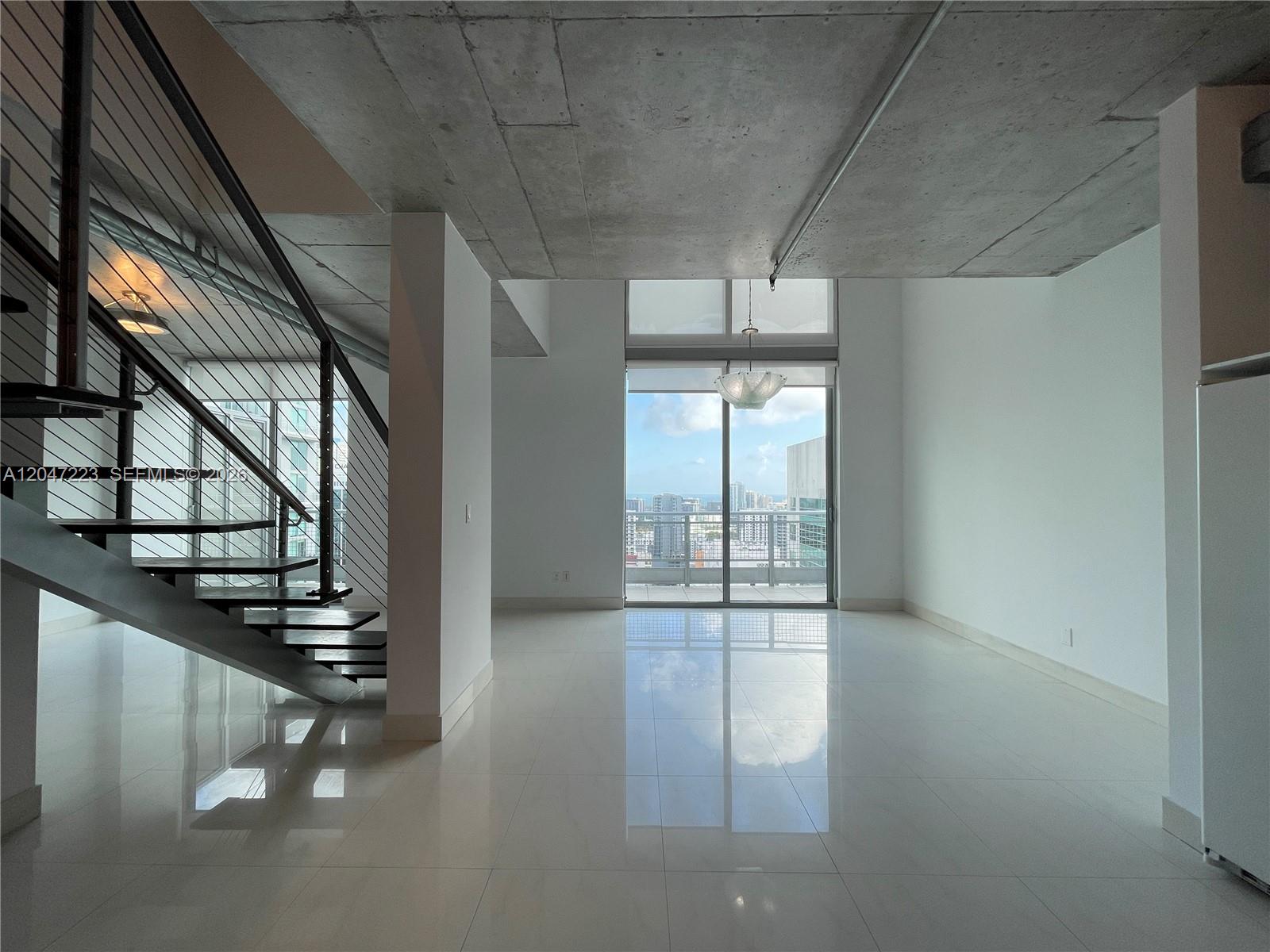 An open living area features a concrete ceiling, white tile floors, and a metal staircase — 690 SW 1st Ct # 3115, Miami FL 33130, MIAMI, FL