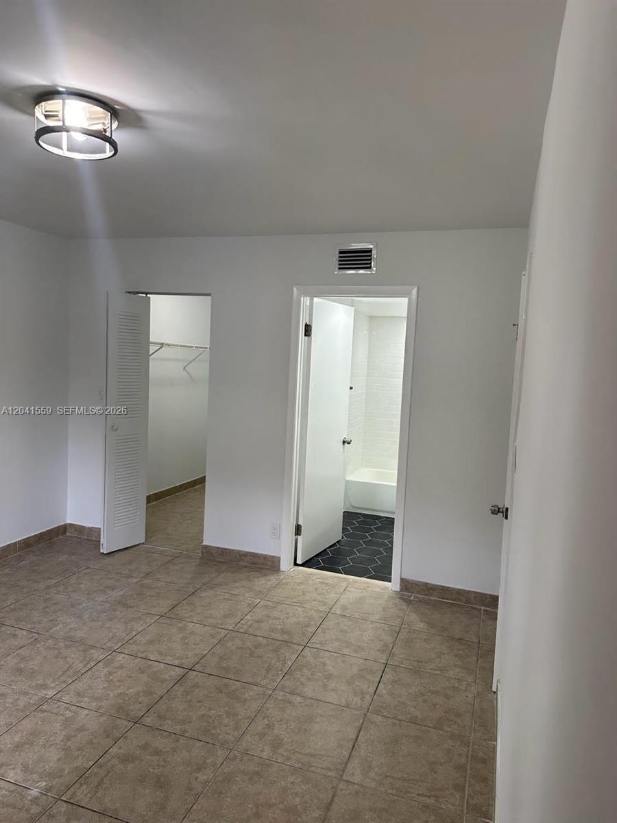 A room with tan tile flooring features a walk-in closet and an attached bathroom — 8100 Geneva Ct # 142, Doral FL 33166, DORAL, FL