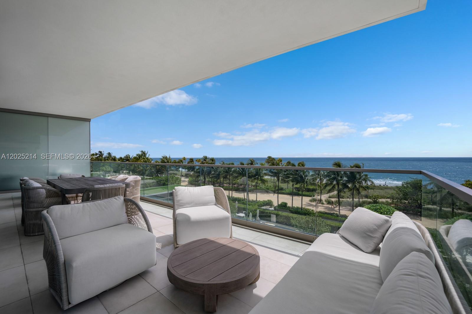 A spacious balcony features modern outdoor furniture overlooking a sandy beach and the ocean — 10203 Collins Ave # 403, Bal Harbour FL 33154, BAL HARBOUR, FL