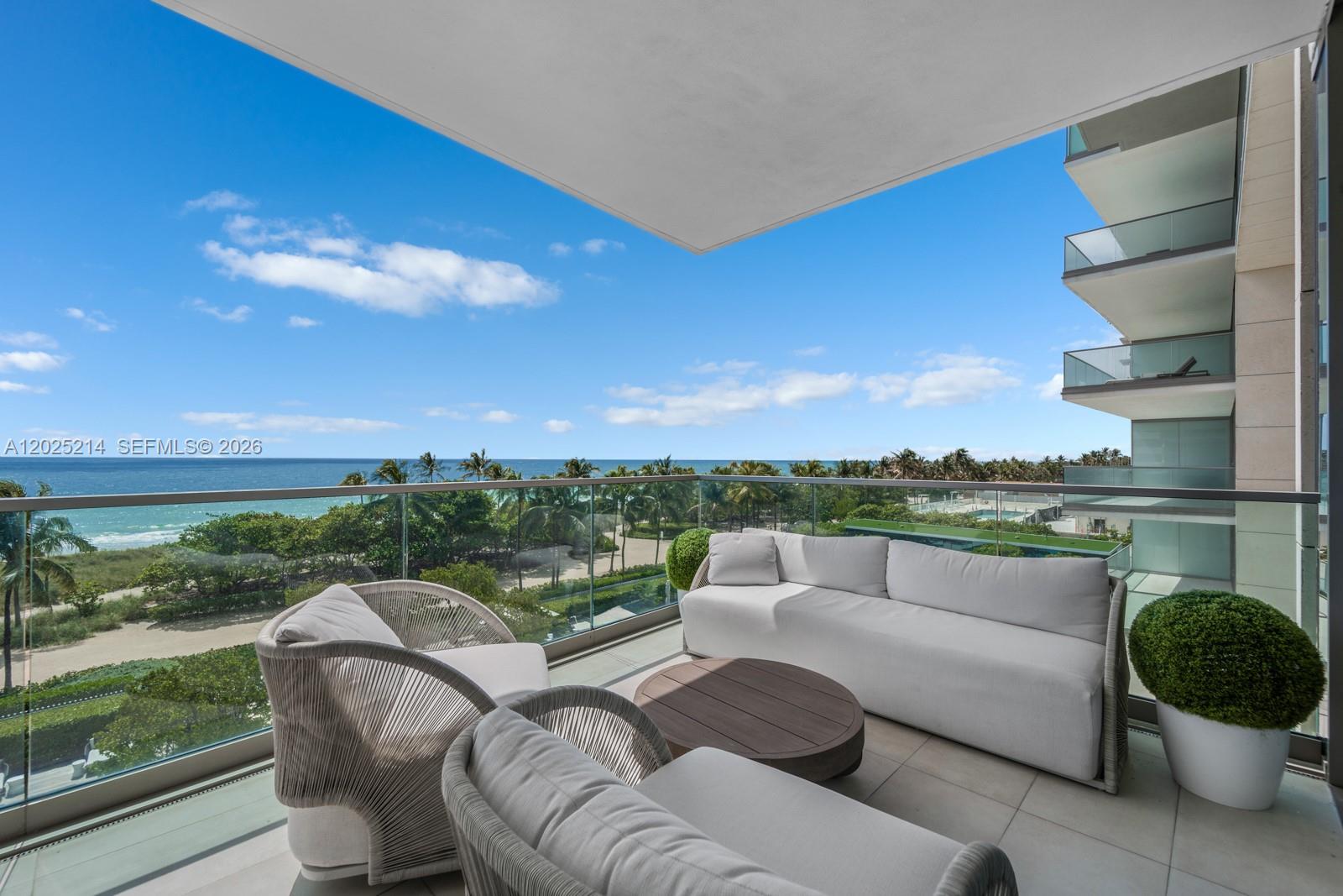 A furnished balcony overlooks the ocean with a glass railing and a white sofa — 10203 Collins Ave # 403, Bal Harbour FL 33154, BAL HARBOUR, FL