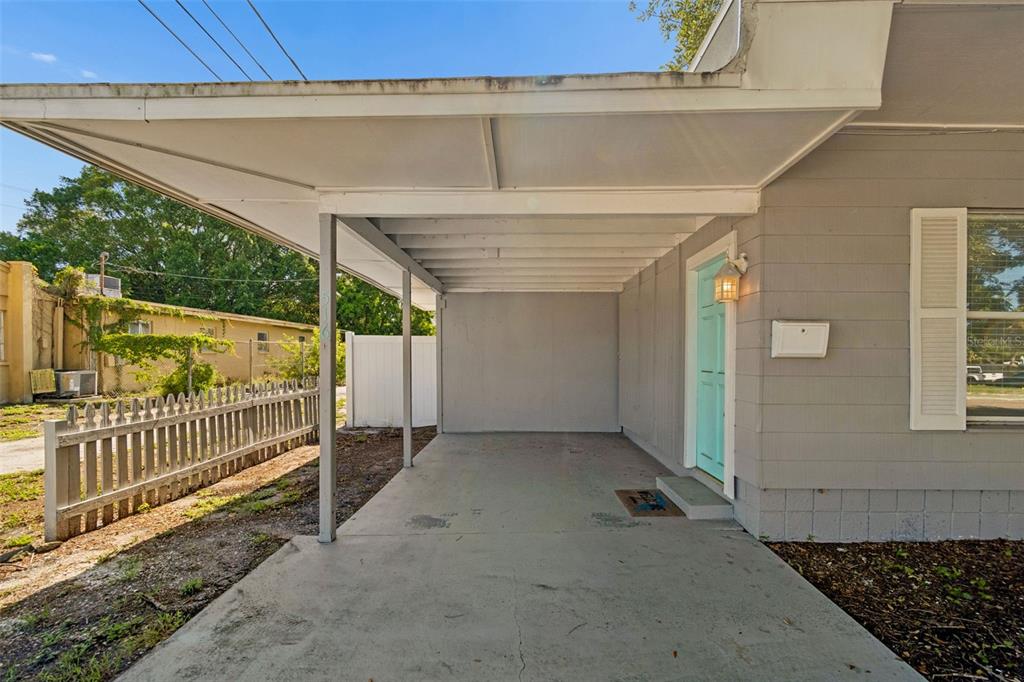 A gray house exterior features a covered carport, a light blue front door, and a fence — 516 64TH STREET S, ST PETERSBURG, FL