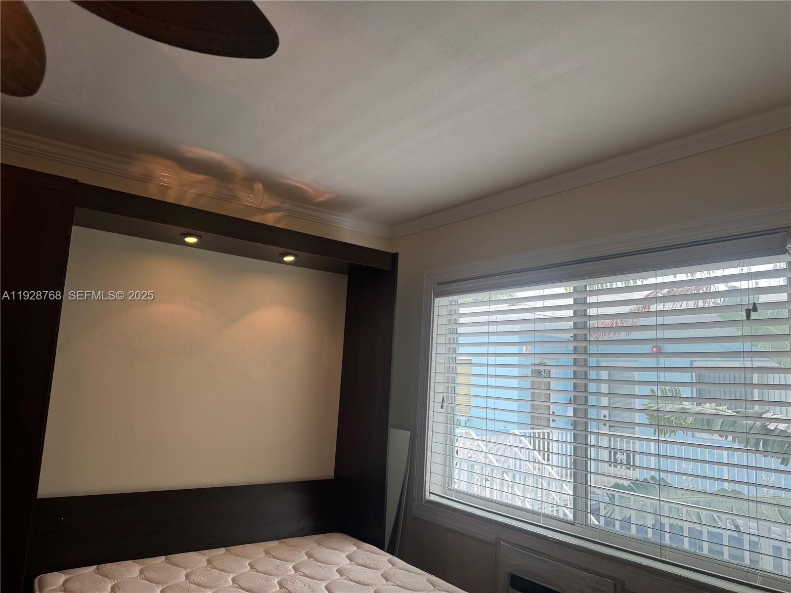 A bedroom features a dark wood headboard unit with recessed lighting and a window — 401 Collins Ave # 21, Miami Beach FL 33139, MIAMI BEACH, FL