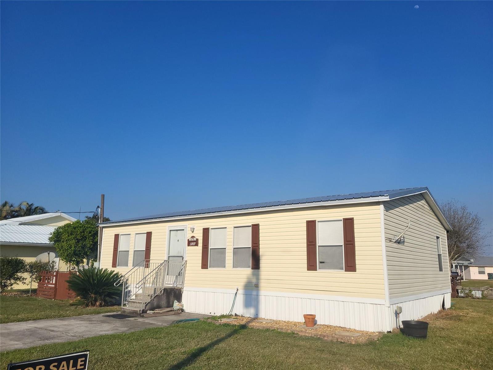 A yellow single-wide mobile home with brown shutters sits on a grassy lot — 1057 Blue Heron, Moore Haven FL 33471, MOORE HAVEN, FL