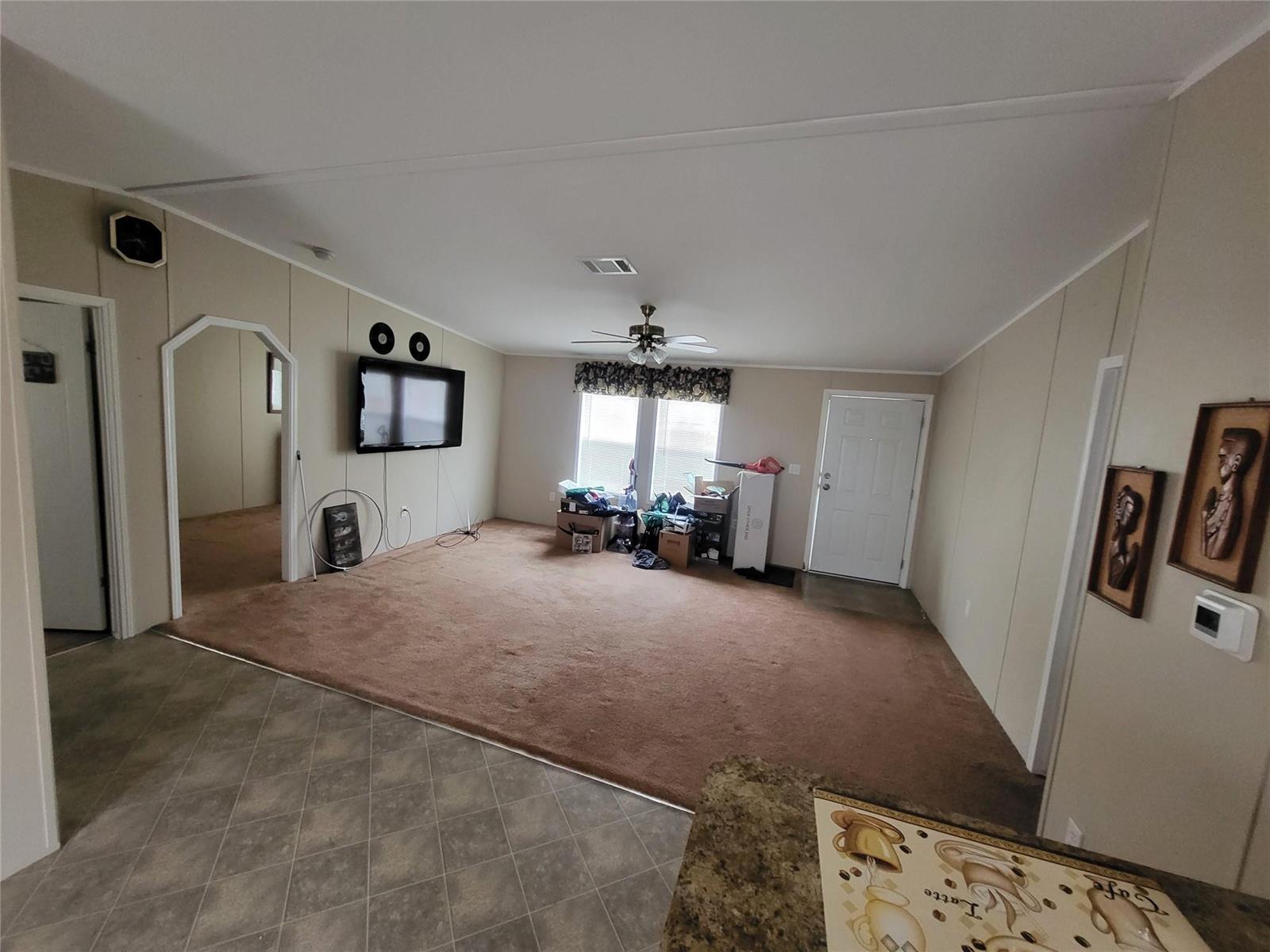 A living room with beige walls, brown carpet, a ceiling fan, and a mounted television — 1057 Blue Heron, Moore Haven FL 33471, MOORE HAVEN, FL