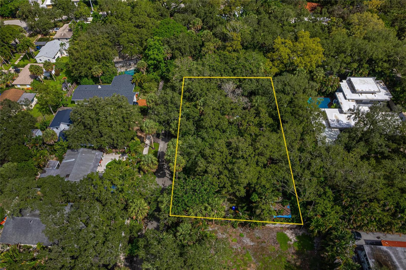 An aerial view shows a rectangular, tree-covered vacant lot outlined in yellow among residential homes — FORT LAUDERDALE, FL
