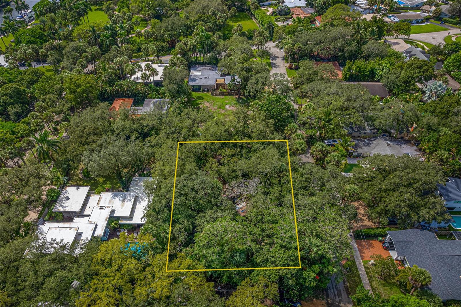 An aerial view shows a rectangular, tree-covered vacant lot outlined in yellow within a neighborhood — FORT LAUDERDALE, FL