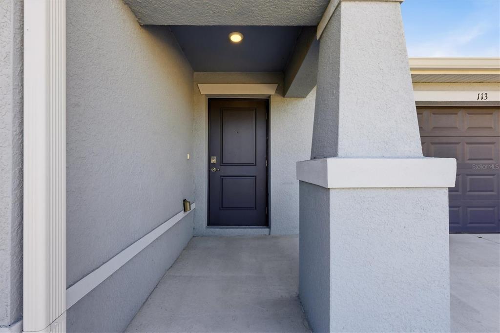 A covered entryway features a dark front door, a concrete porch, and a garage door — 113 LILYAN COURT, ROTONDA WEST, FL