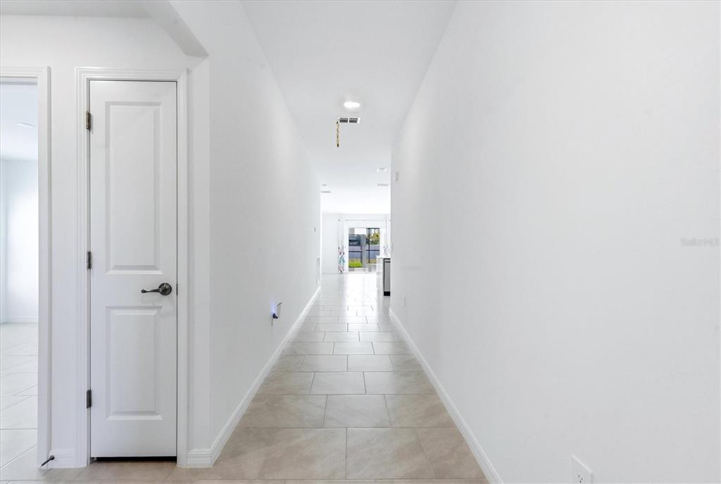 A long, white hallway with light-colored tile flooring leads toward a bright doorway — 113 LILYAN COURT, ROTONDA WEST, FL