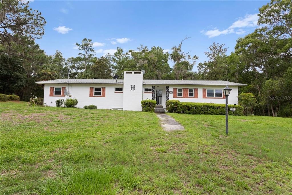 A single-story white house with a brick chimney and a large grassy front yard — 23363 NW 191ST AVENUE, HIGH SPRINGS, FL