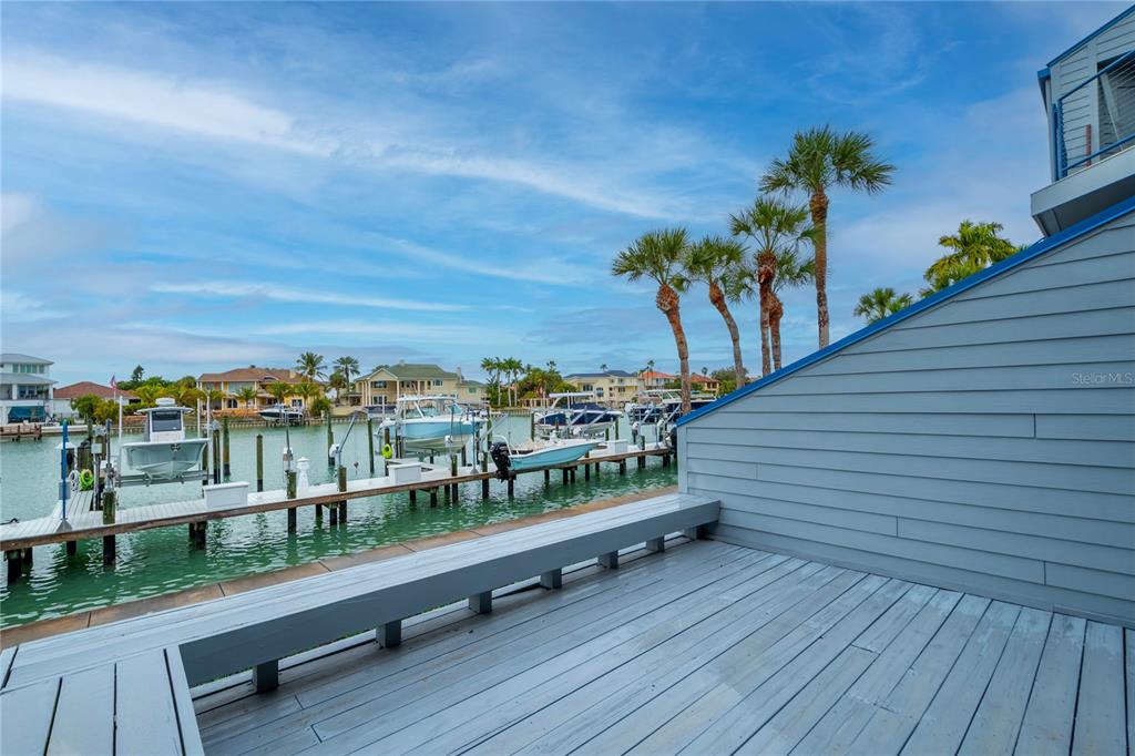 A wooden deck overlooks a canal with boat slips and palm trees under a blue sky — 900 PINELLAS BAYWAY S UNIT 109, TIERRA VERDE, FL