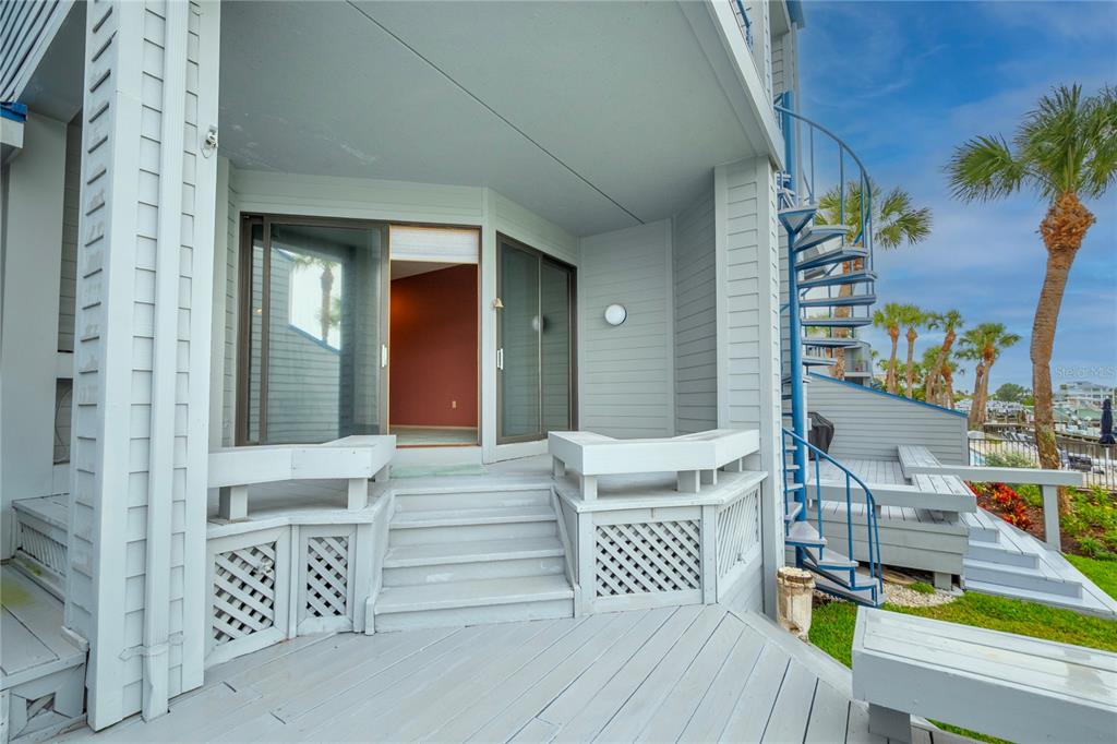 A light gray wooden deck features a spiral staircase, built-in benches, and sliding glass doors — 900 PINELLAS BAYWAY S UNIT 109, TIERRA VERDE, FL