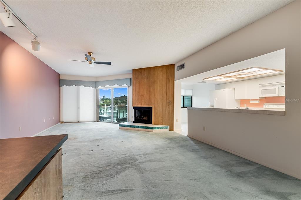 A living room features a wood-paneled fireplace, light blue carpet, and a view of water — 900 PINELLAS BAYWAY S UNIT 109, TIERRA VERDE, FL