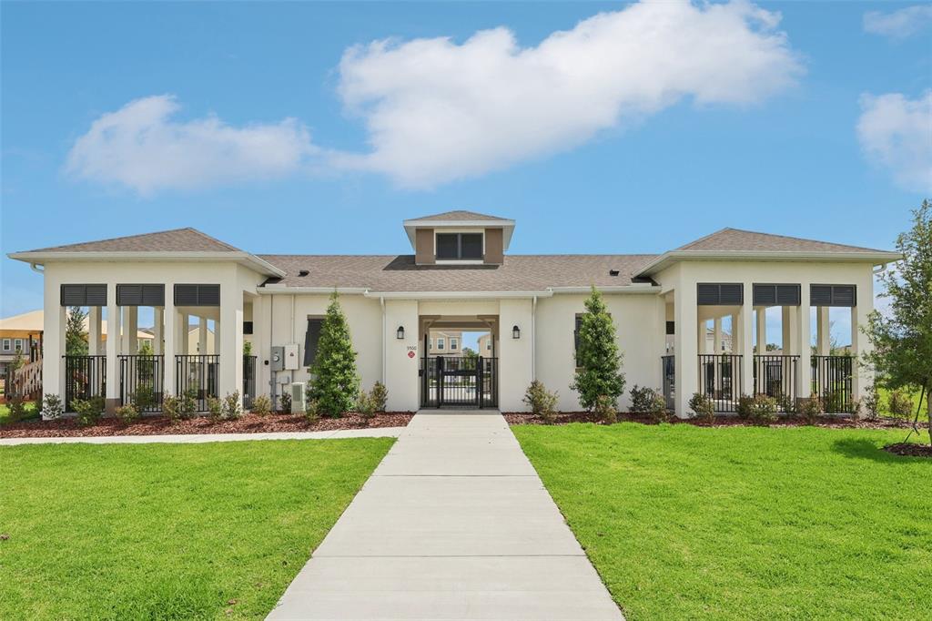 A single-story building with a central gated entrance and covered side patios under a blue sky — 1813 LATTICE WAY, ST CLOUD, FL