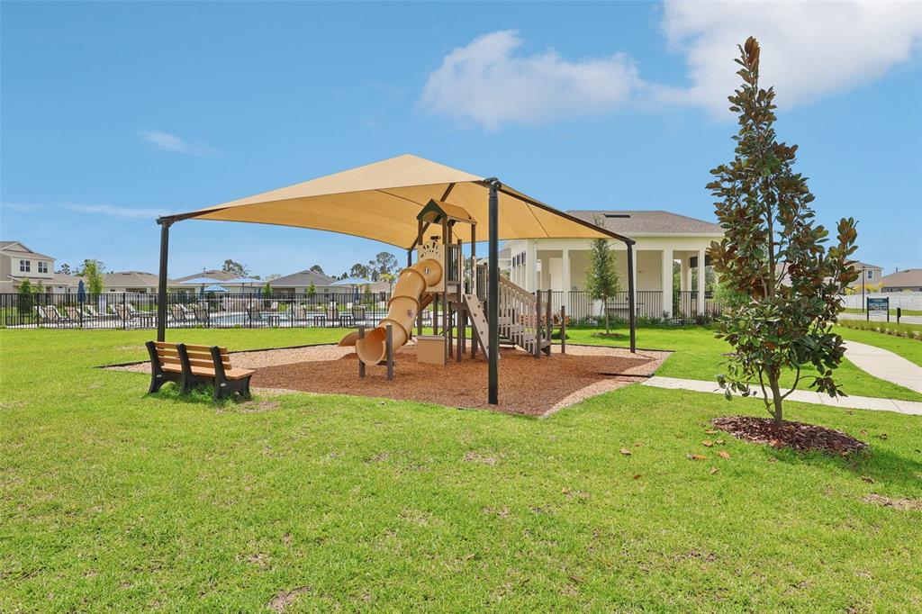 A playground with a slide and shade canopy sits on a grassy lawn near houses — 1813 LATTICE WAY, ST CLOUD, FL