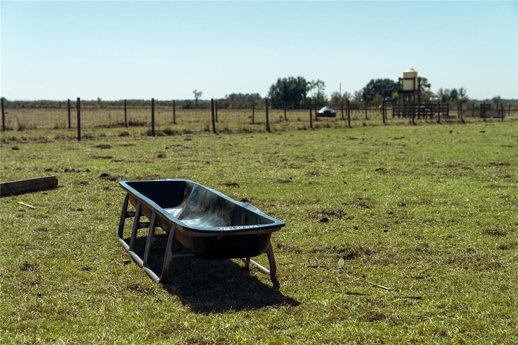 A black livestock trough sits in a large, fenced grassy pasture under a clear sky — 1200 ARBUCKLE BRANCH ROAD, SEBRING, FL