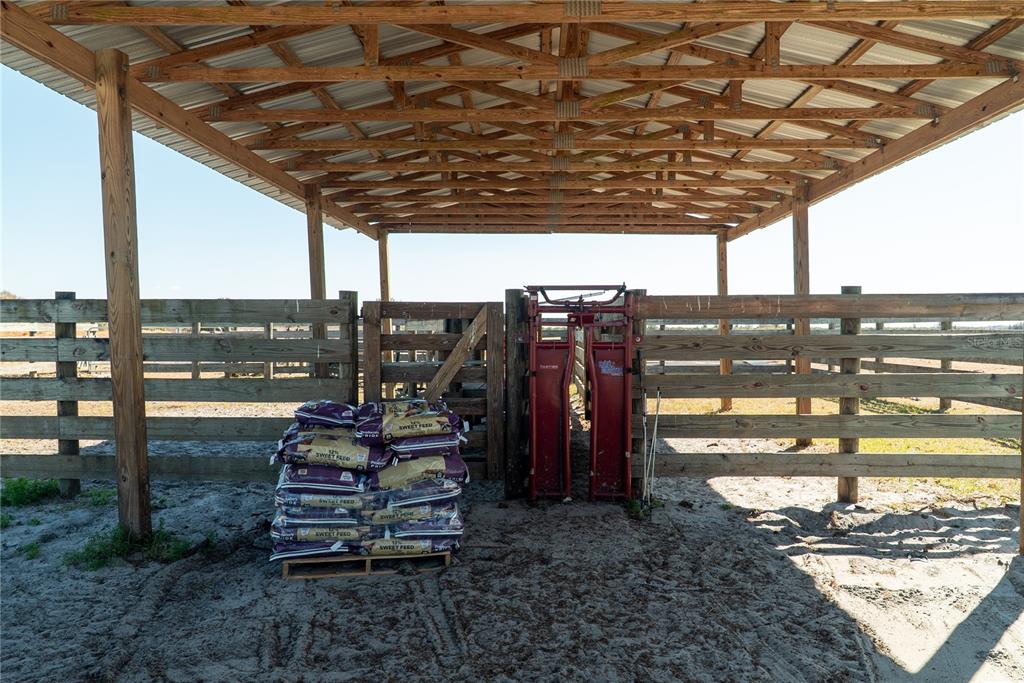A covered outdoor livestock pen features a wooden fence, a metal squeeze chute, and feed bags — 1200 ARBUCKLE BRANCH ROAD, SEBRING, FL