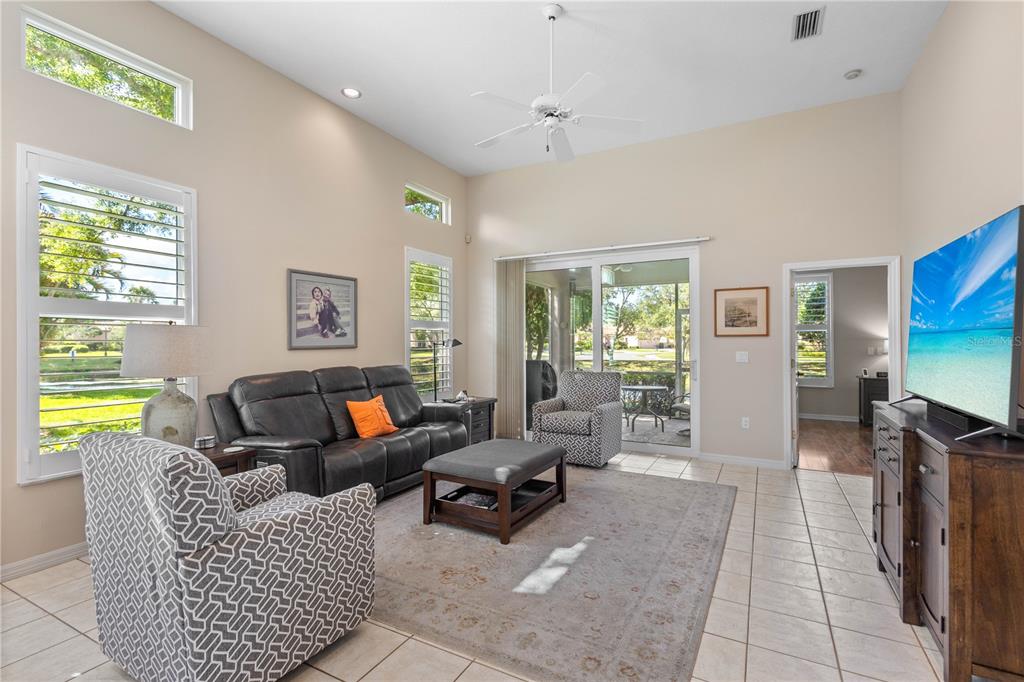 A living room features a vaulted ceiling, tile flooring, a leather sofa, and sliding glass doors — 7106 LA RONDA COURT, SARASOTA, FL