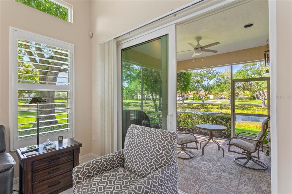 A living room with a patterned armchair looks out through sliding doors to a screened patio — 7106 LA RONDA COURT, SARASOTA, FL