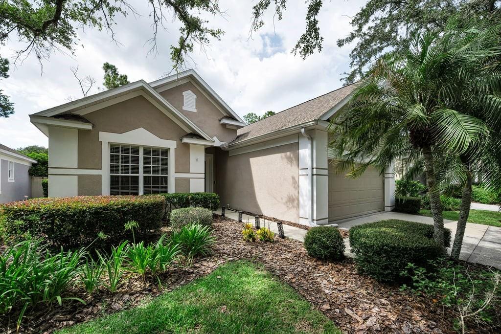 A tan single-story house with a two-car garage, white trim, and landscaped front yard — 18104 HAMDEN PARK WAY, TAMPA, FL