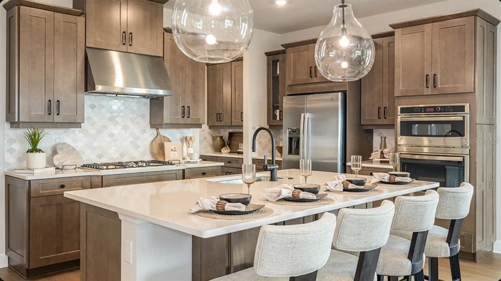 A kitchen features wood cabinets, a large white island with seating, and stainless steel appliances — 7825 CENTAURUS WAY, SARASOTA, FL