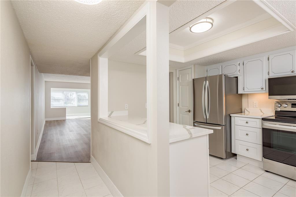 A kitchen with white cabinets and stainless steel appliances opens to a living area — 8 GLENCOE PLACE UNIT 104, DUNEDIN, FL