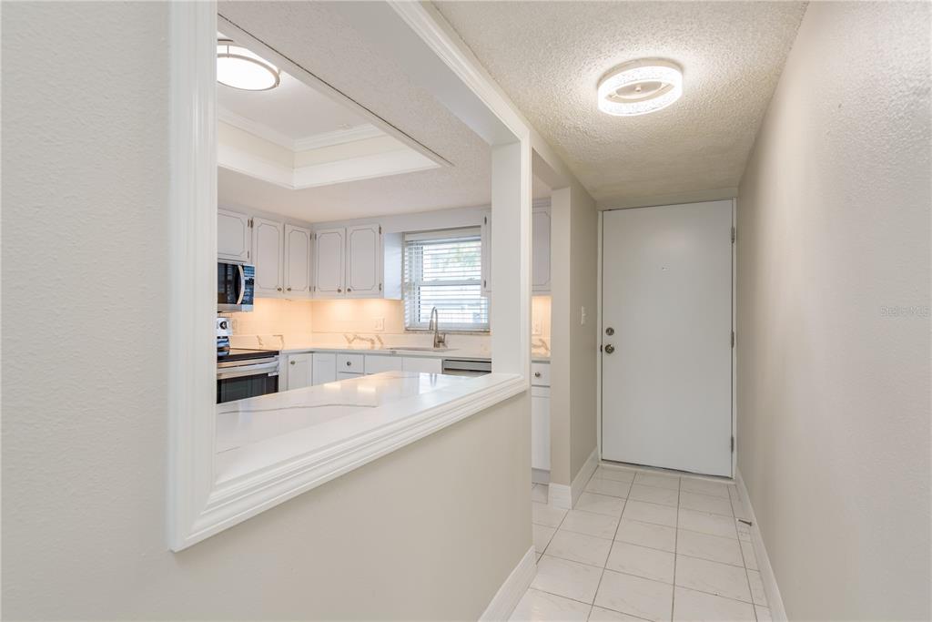 A view from a tiled entryway looking into a kitchen with white cabinets and countertops — 8 GLENCOE PLACE UNIT 104, DUNEDIN, FL