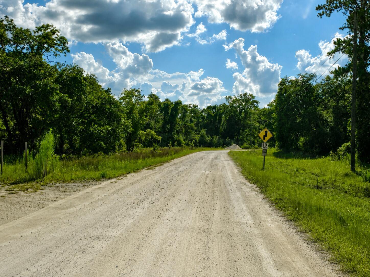 A dirt road leads through a wooded area under a bright, cloudy blue sky — 6600 150th Place, FL 32094, FL