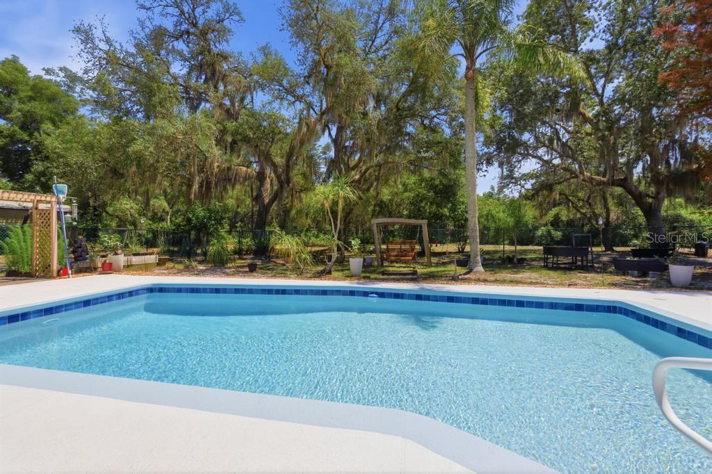 A rectangular swimming pool sits in a backyard with mature trees and a wooden swing — 2514 KRINKLEWOOD DRIVE, DELAND, FL