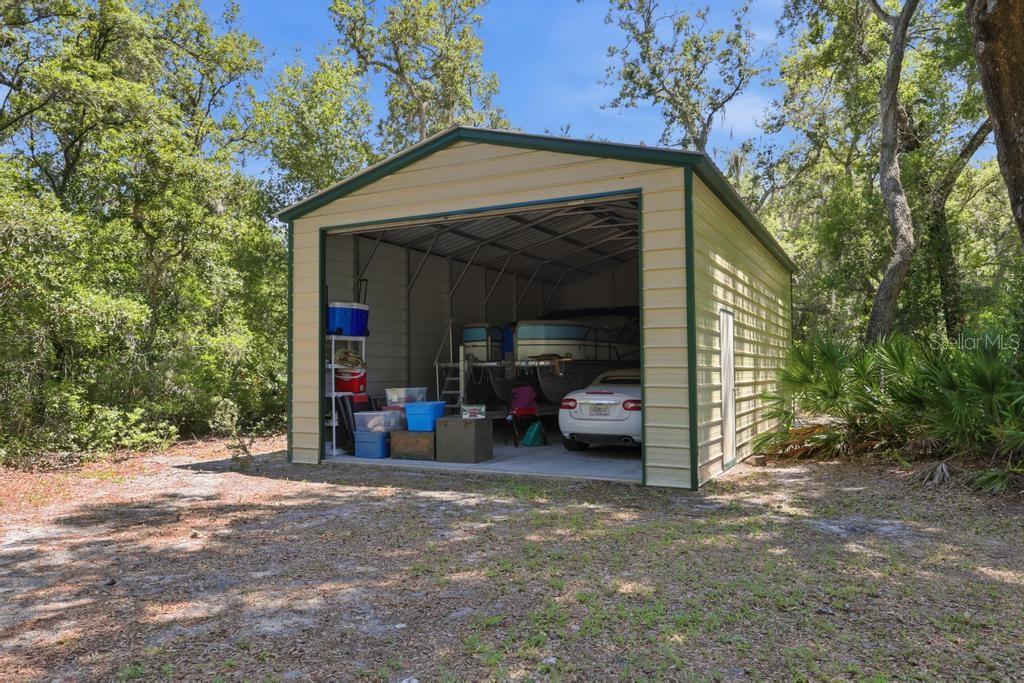 A detached metal storage shed with an open garage door sits in a wooded area — 2514 KRINKLEWOOD DRIVE, DELAND, FL