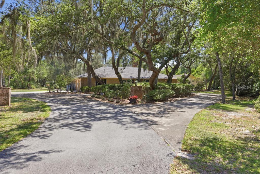A split driveway leads to a single-story house surrounded by large, moss-draped oak trees — 2514 KRINKLEWOOD DRIVE, DELAND, FL