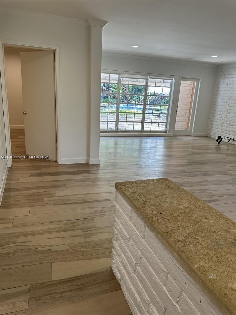 An interior view shows a room with light wood-look tile flooring and a white brick wall — BAL HARBOUR, FL