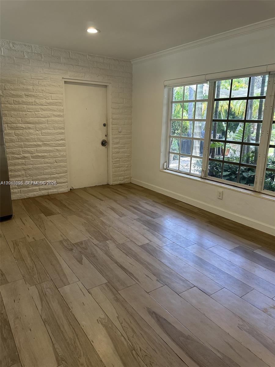 This room features white painted brick walls, wood-look tile flooring, and a large window — BAL HARBOUR, FL
