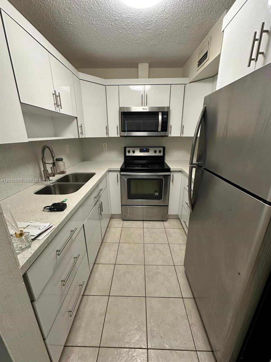 A galley kitchen features white cabinets, stainless steel appliances, and light-colored tile flooring — 6675 W 4th Ave # 310, Hialeah FL 33012, HIALEAH, FL